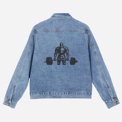 The back view of a blue denim jacket featuring a striking black graphic on the back depicts a knight in armor powerfully deadlifting a barbell against a plain white background, blending medieval style with modern flair. 