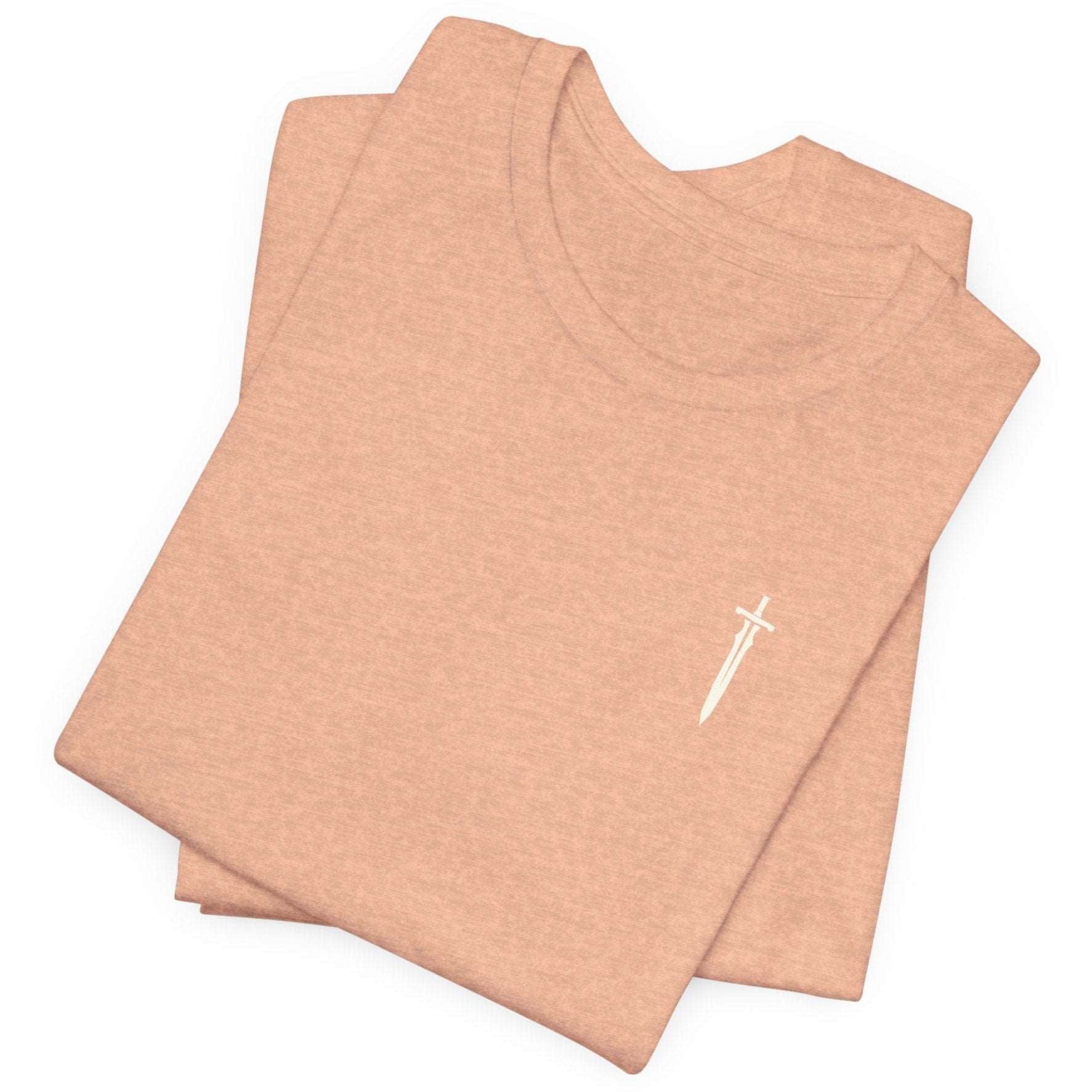 A folded plain light brown t-shirt featuring a small white sword graphic on the upper left chest, evoking a subtle medieval aesthetic. 