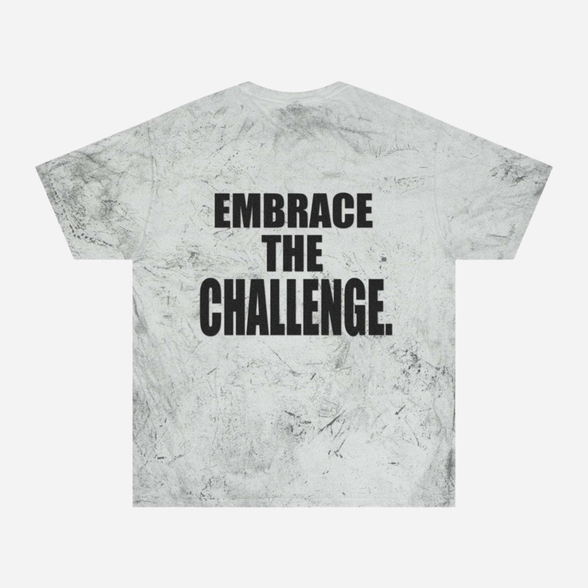 A gray tie-dye t-shirt with a textured pattern reminiscent of a medieval shirt, featuring a motivational message in bold black letters that reads "Embrace the Challenge" on the back.